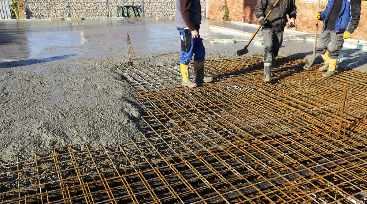 Equipe espalhando concreto sobre a malha de aço de um piso